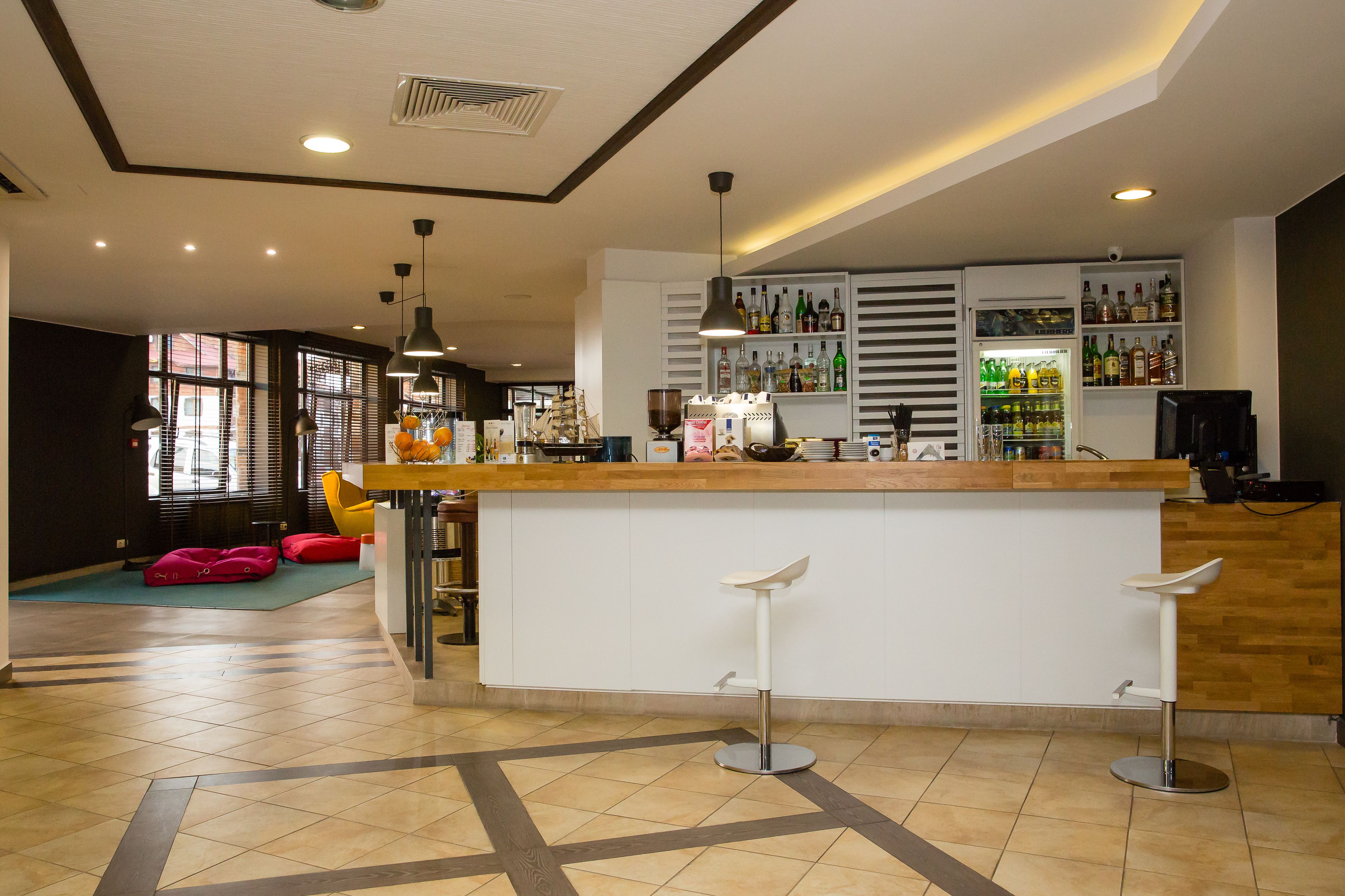 Uma área de bar moderna com balcão de madeira, banquetas brancas e variedade de garrafas nas prateleiras.