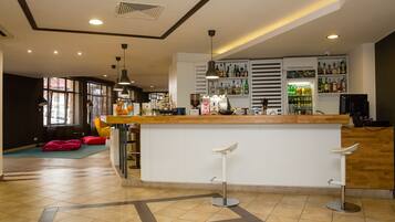 Uma área de bar moderna com balcão de madeira, banquetas brancas e variedade de garrafas nas prateleiras.