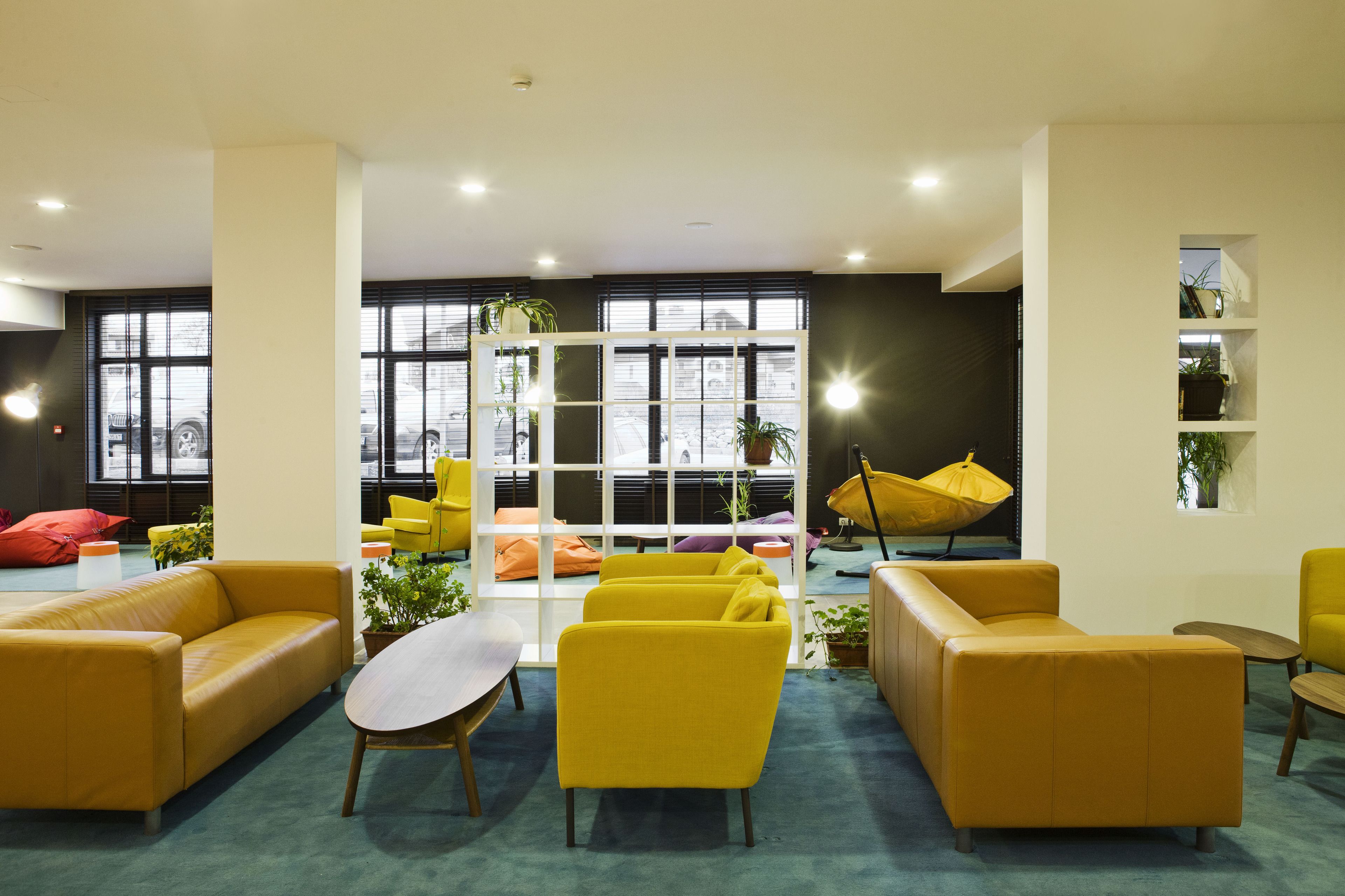 A modern lounge area with yellow sofas, a wooden coffee table, and potted plants.