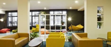 A modern lounge area with yellow sofas, a wooden coffee table, and potted plants.