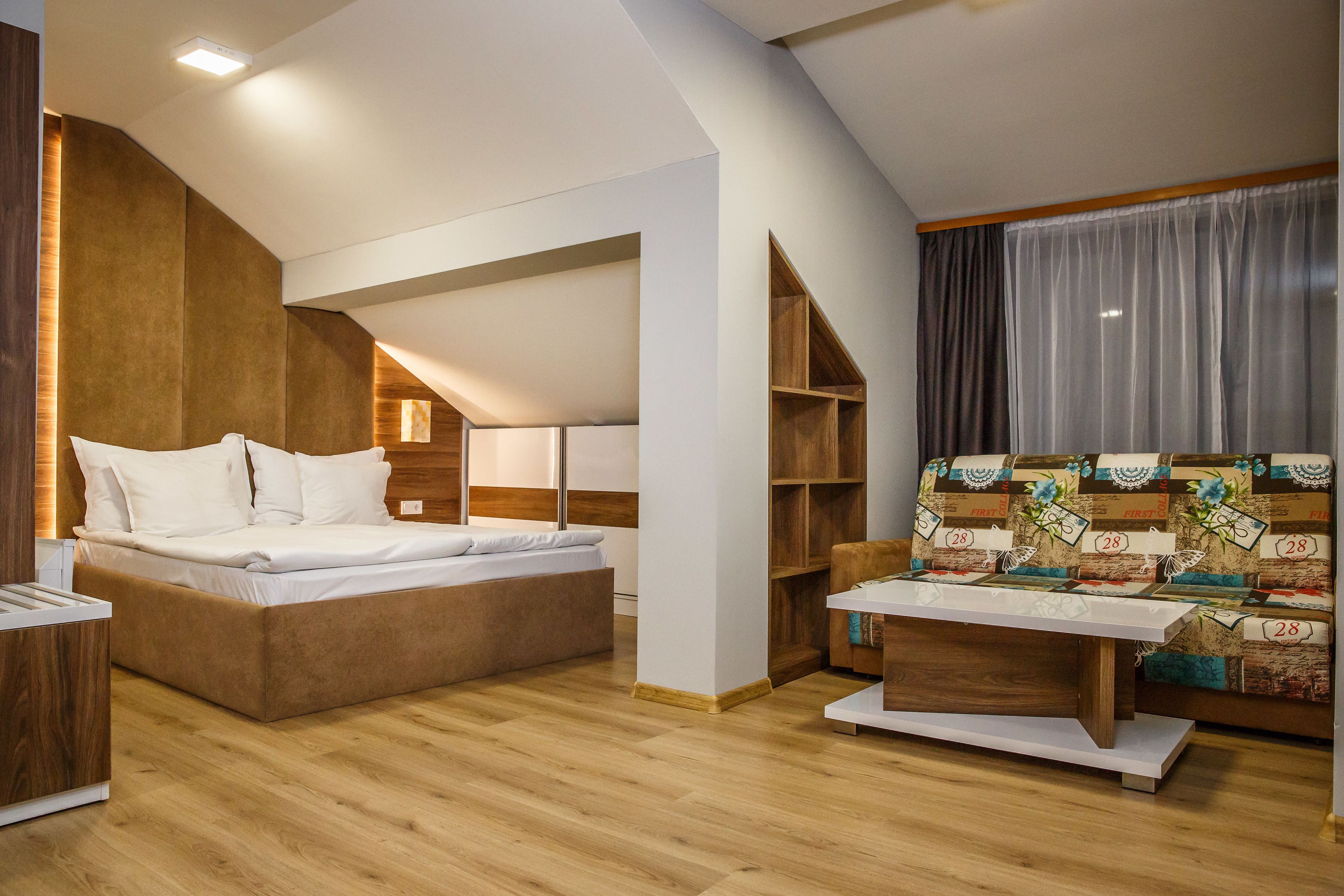 A modern bedroom with a loft bed, a wooden nightstand, a small table, and a sofa with patterned cushions.