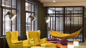 Un interior moderno con sillones amarillos, una hamaca y un ventanal con persianas.