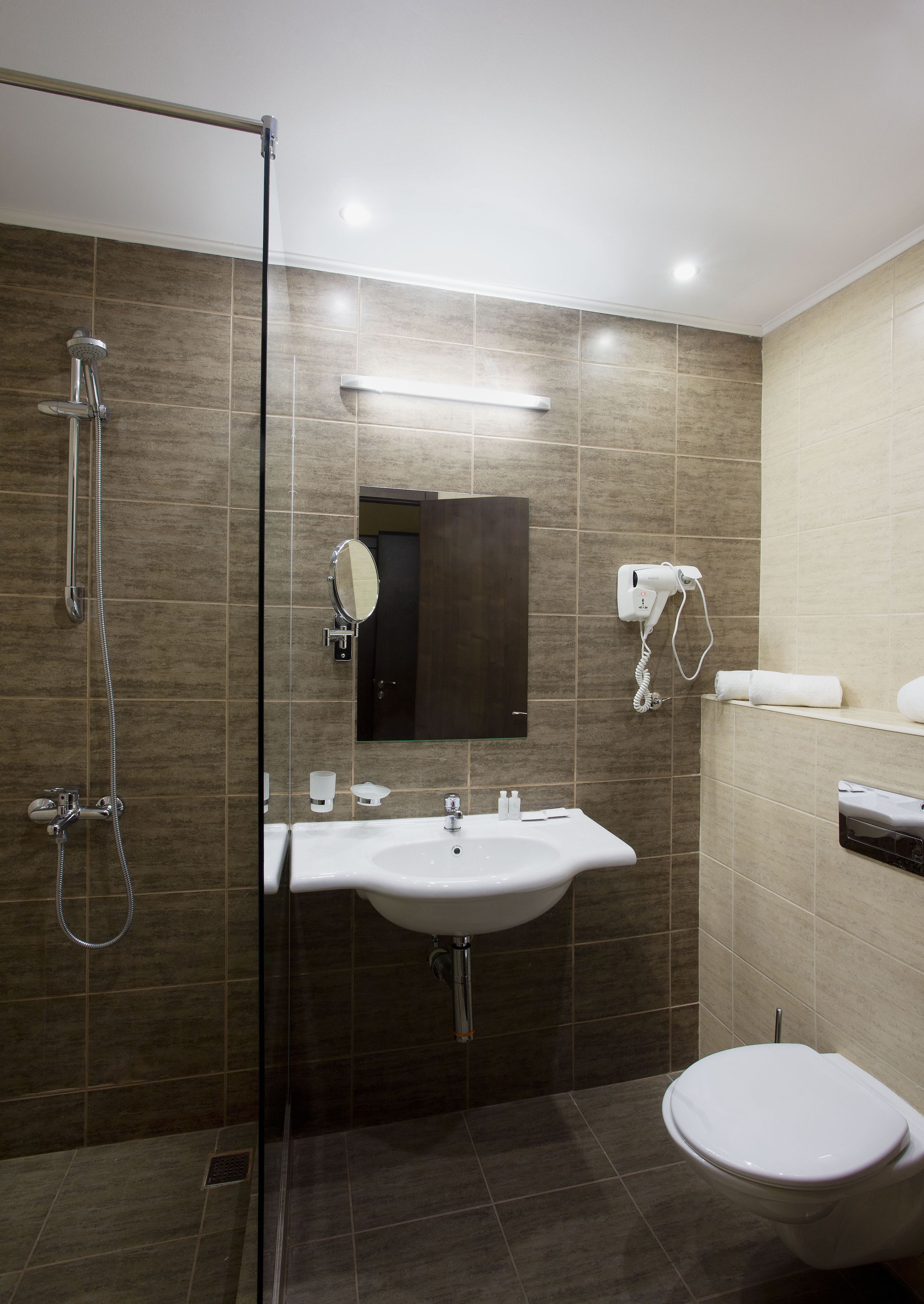 A modern bathroom with a glass-enclosed shower, a white sink, a mirror, and a toilet.