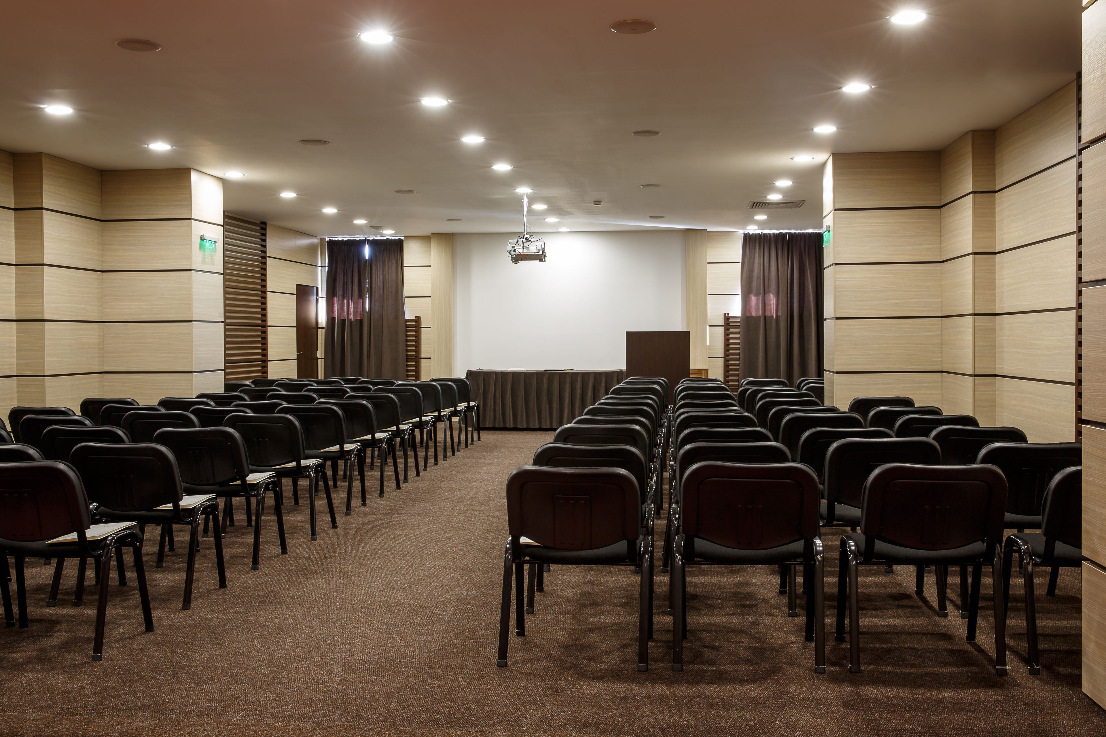 Un salón de conferencias con filas de sillas, un atril y suelo alfombrado.
