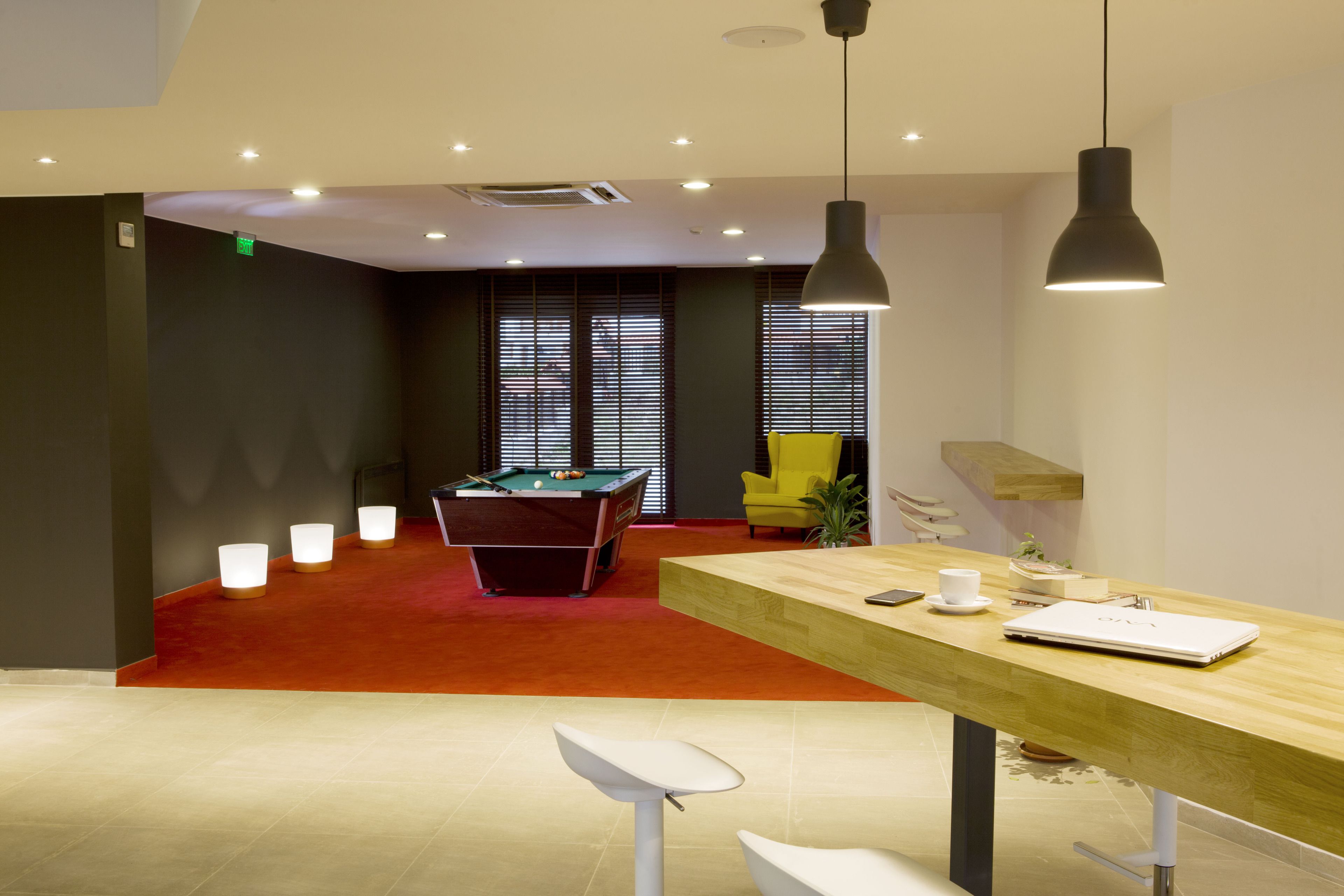 Een moderne ruimte met een pooltafel, een houten tafel met een laptop en een gele stoel.
