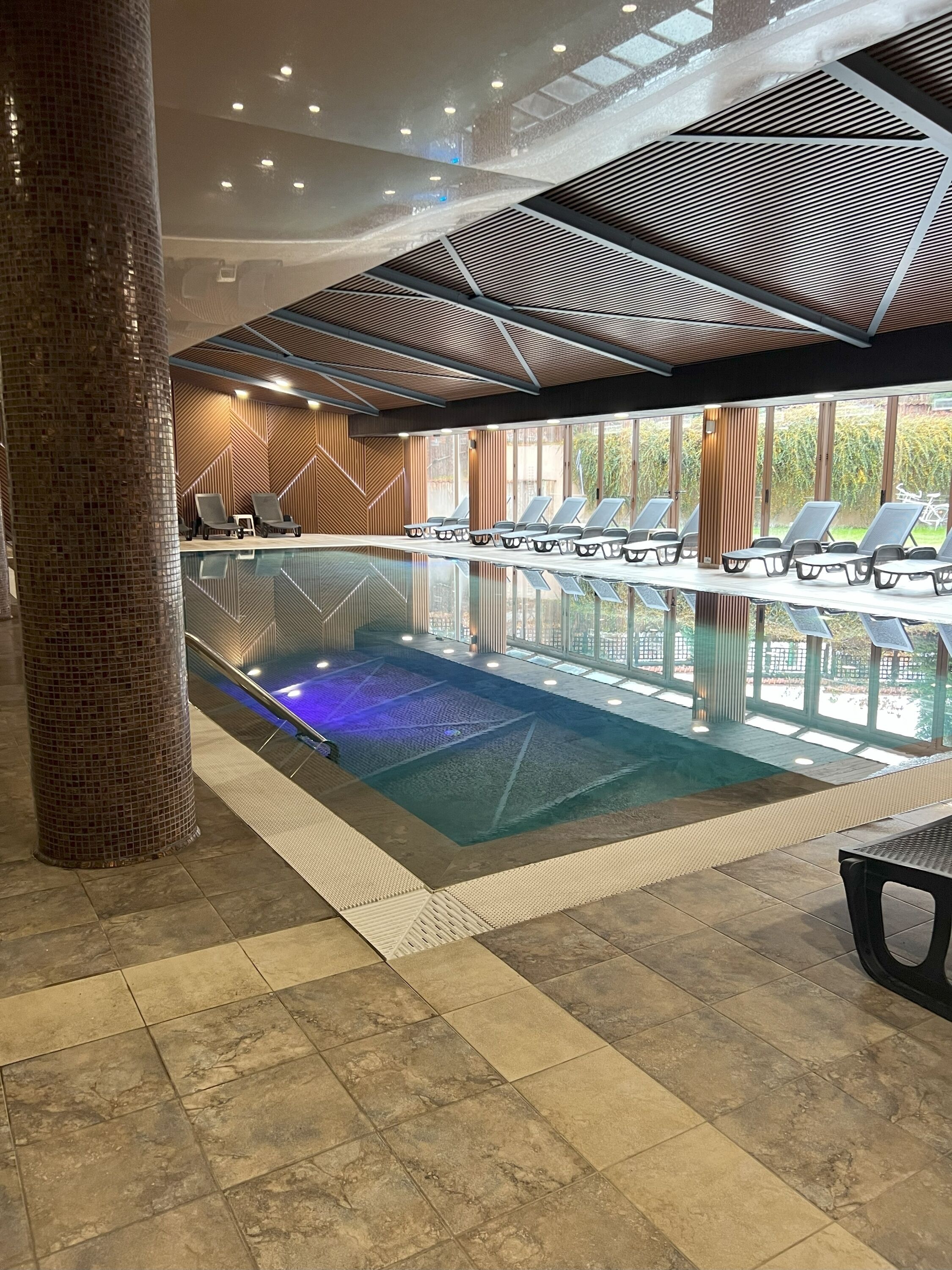 An indoor swimming pool with lounge chairs and a tiled floor.