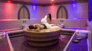 Un spa con una pared cubierta de mosaicos, un jacuzzi circular y una persona recostada en él.