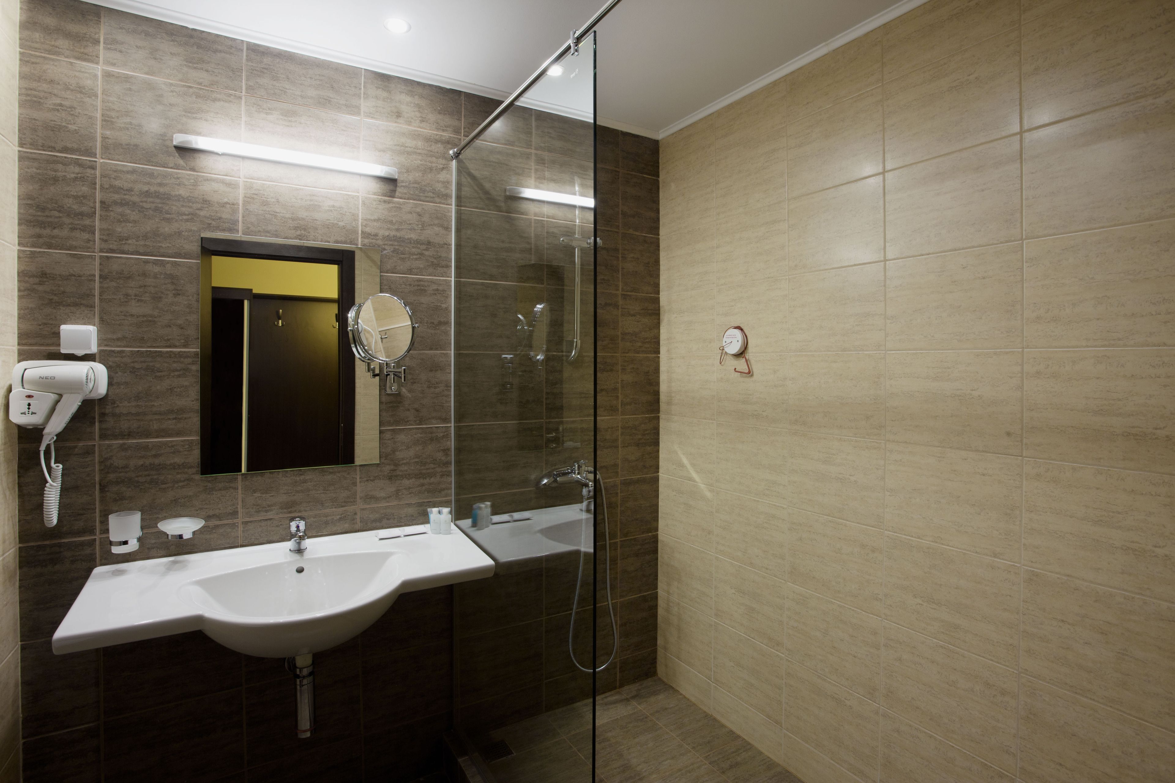 A modern bathroom with a glass shower enclosure, a sink with a mirror, and a hairdryer on the wall.