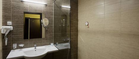 A modern bathroom with a glass shower enclosure, a sink with a mirror, and a hairdryer on the wall.