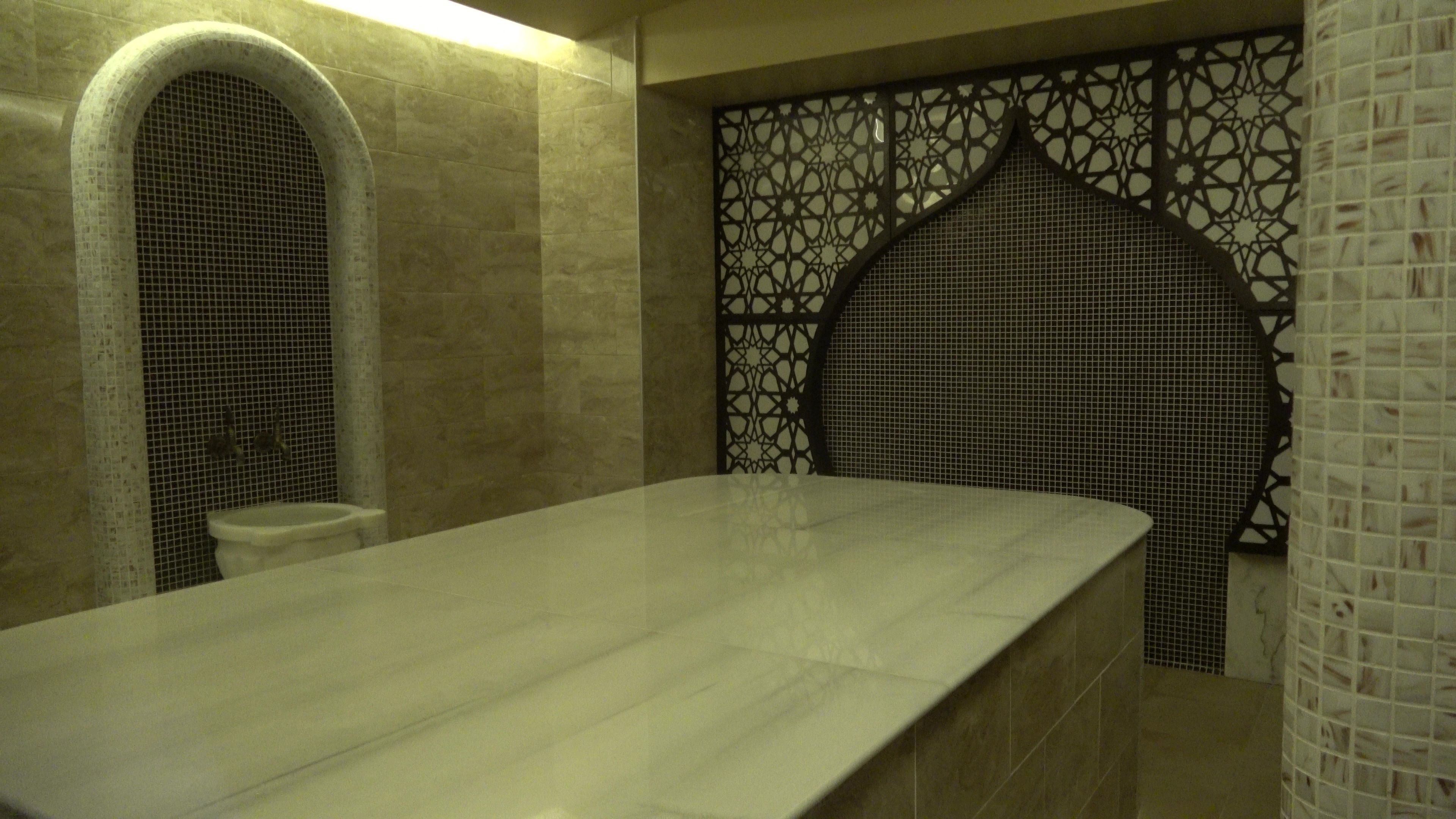 Un baño con lavamanos de mármol, inodoro y un revestimiento de pared decorativo con diseños intrincados.