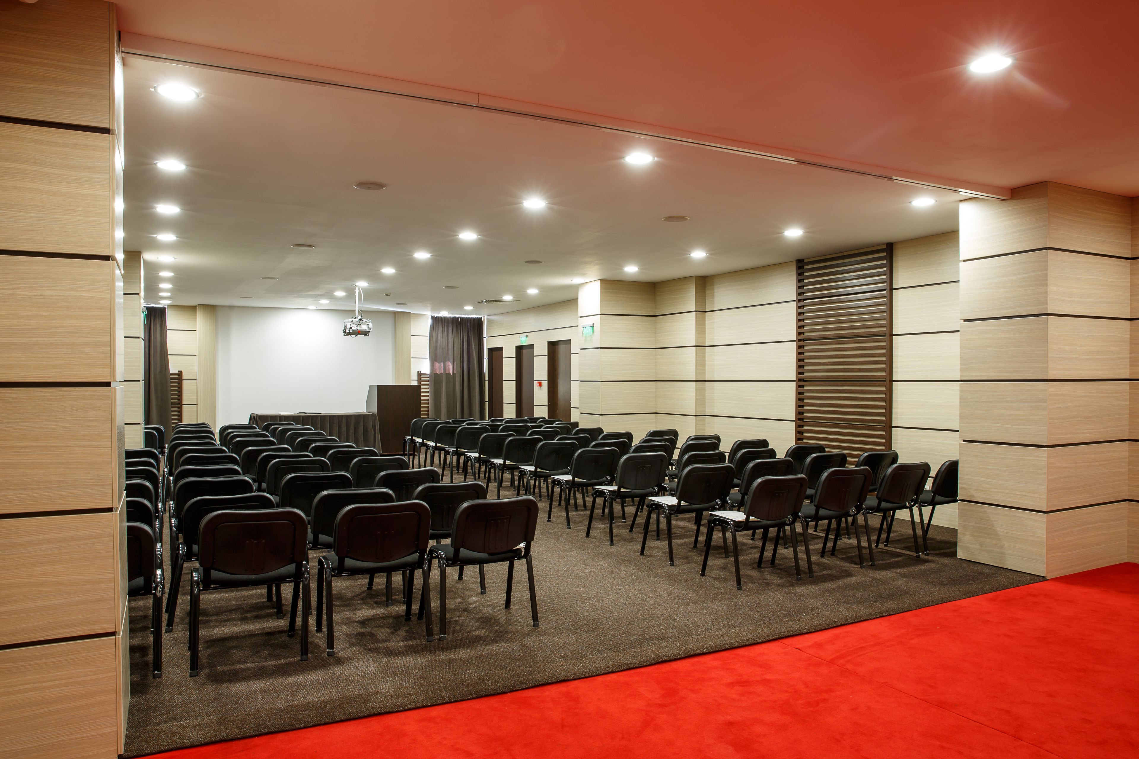 A conference room with rows of chairs, a red carpet, and a wooden panel wall.