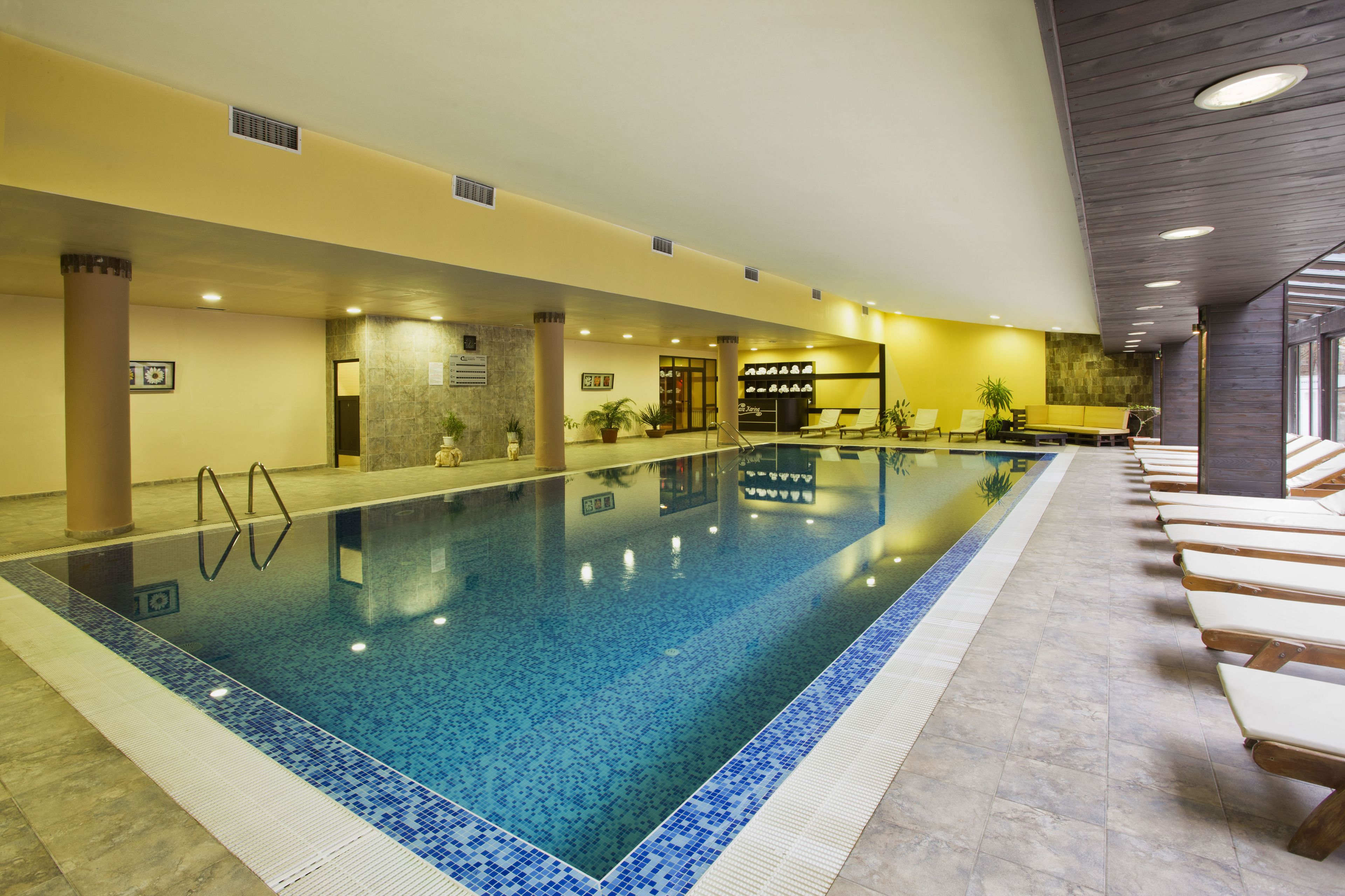 An indoor swimming pool with clear blue water, surrounded by lounge chairs and potted plants.