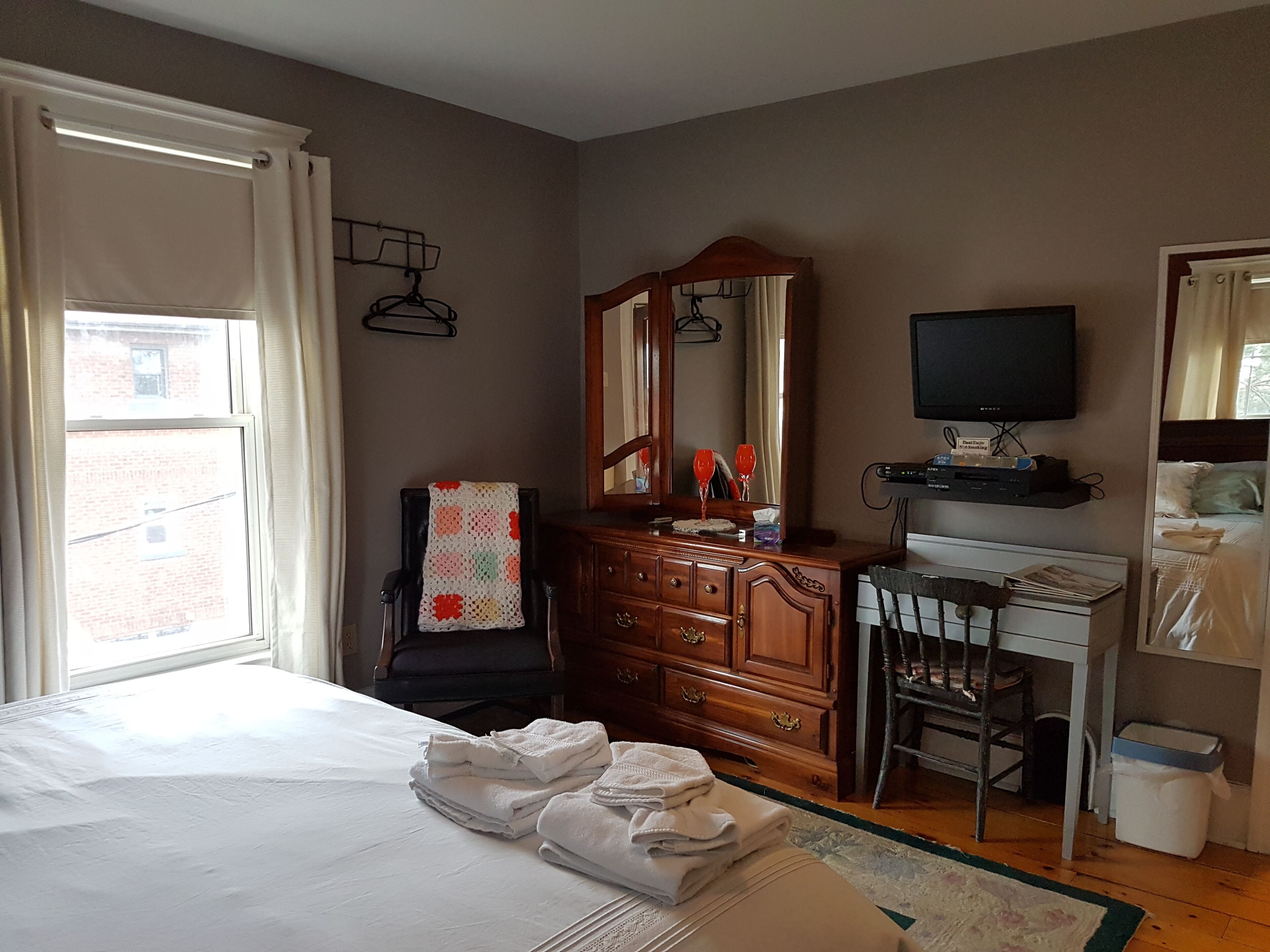 Un dormitorio con cama, escritorio, cómoda, televisor y ventana con cortinas.