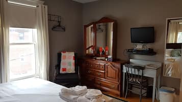 Un dormitorio con cama, escritorio, cómoda, televisor y ventana con cortinas.