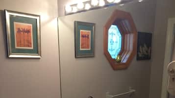 A bathroom with a large mirror, two framed pictures, a sink, a vanity, and a towel dispenser.