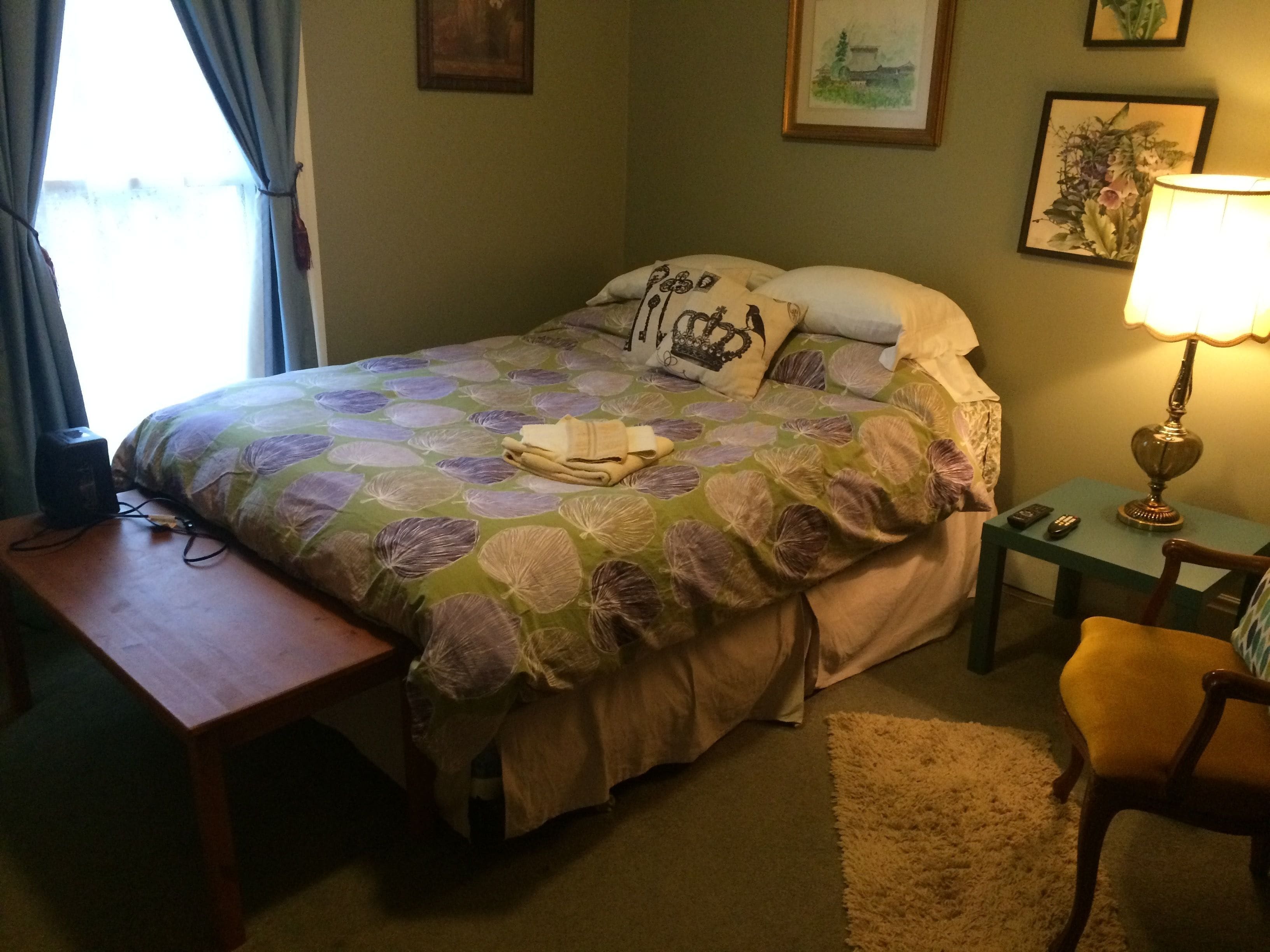 Een netjes ingerichte slaapkamer met een bed, nachtkastje, stoel, lamp en kunstwerken aan de muren.