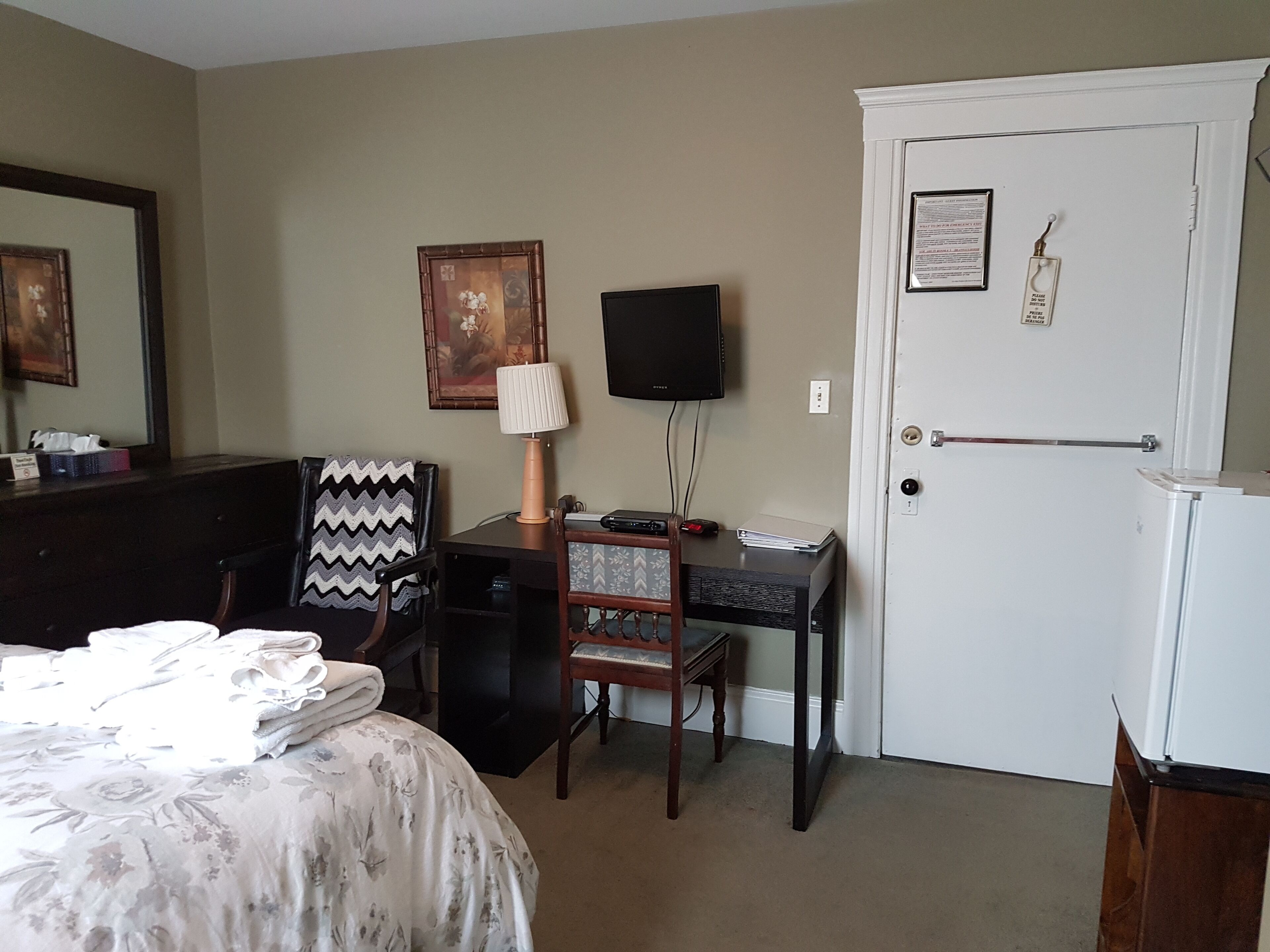 Habitación de hotel con cama, escritorio con lámpara, silla, televisor y puerta con cerradura.