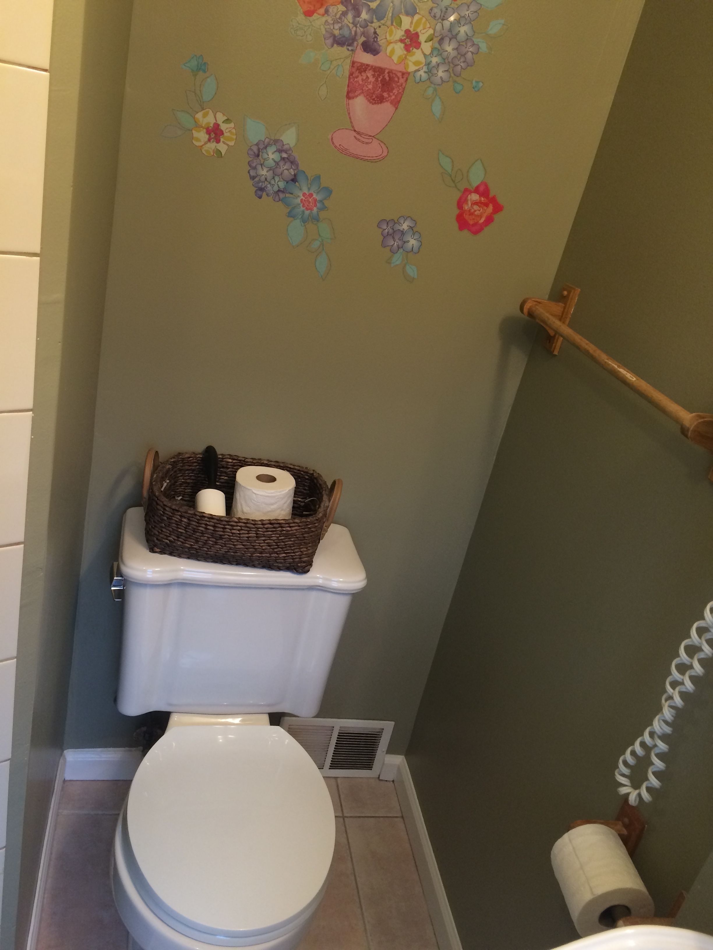 Un baño con un inodoro, un cesto de artículos de aseo y un dispensador de papel higiénico en la pared.