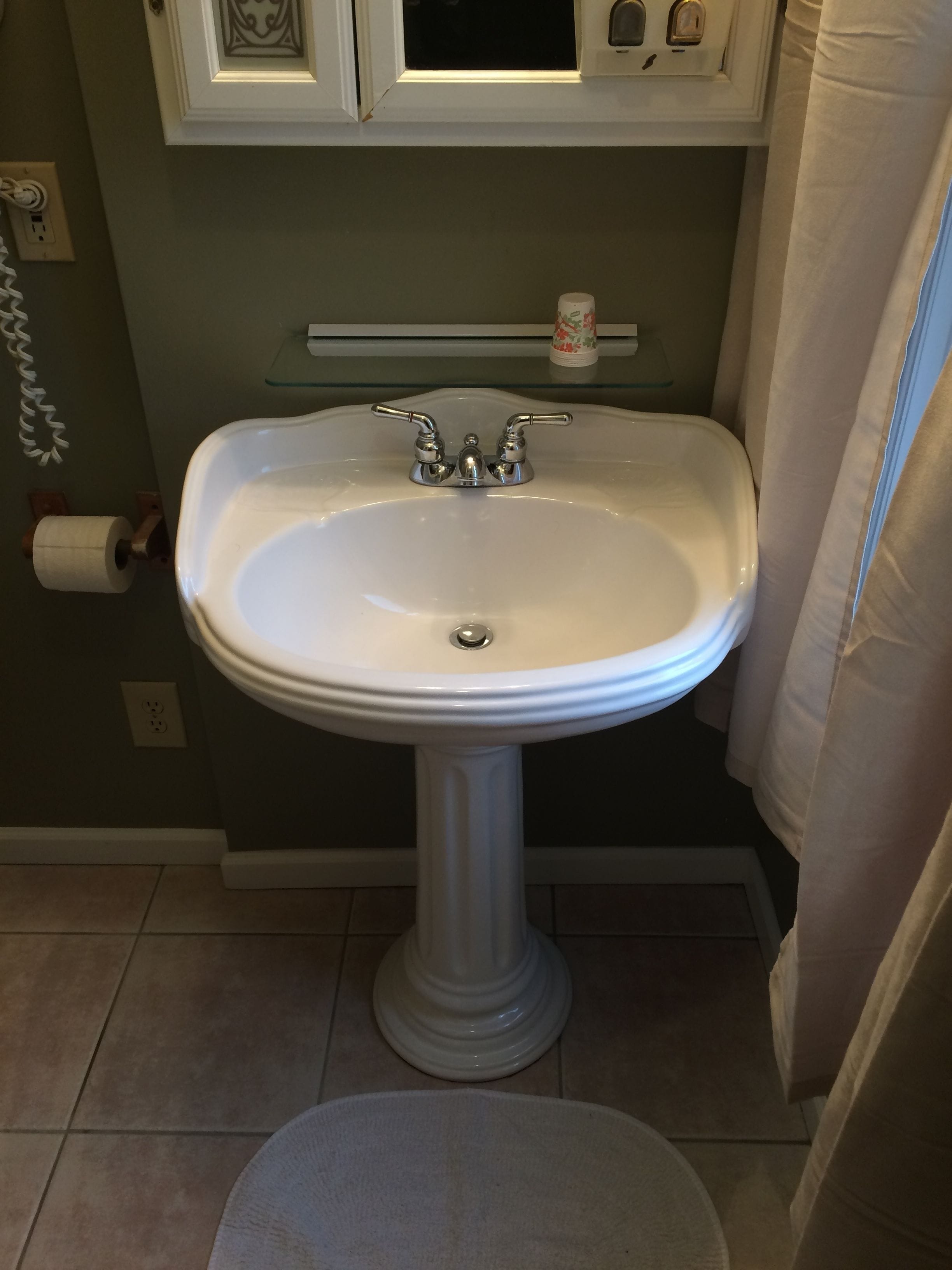 Une salle de bain avec un lavabo sur colonne, des toilettes et une étagère en verre au-dessus du lavabo.
