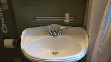 Une salle de bain avec un lavabo sur colonne, des toilettes et une étagère en verre au-dessus du lavabo.