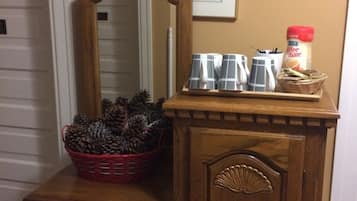 Uma cômoda de madeira com espelho, um cesto de pinhas e uma cafeteira em cima.