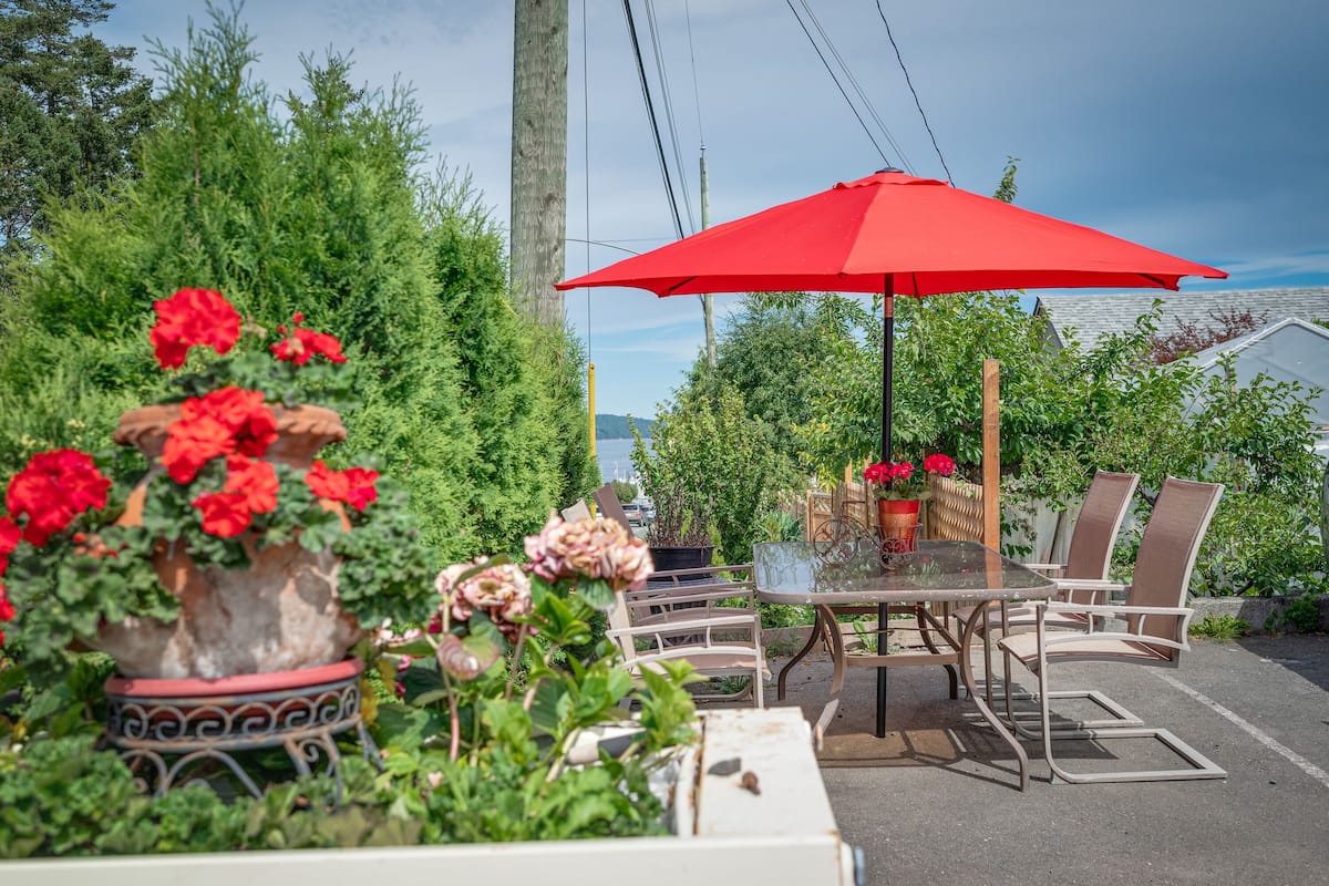 An outdoor patio with a table and chairs, surrounded by potted plants and a red umbrella.