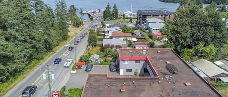 A motel with a red roof, located near a road with parked cars and a marina in the background.