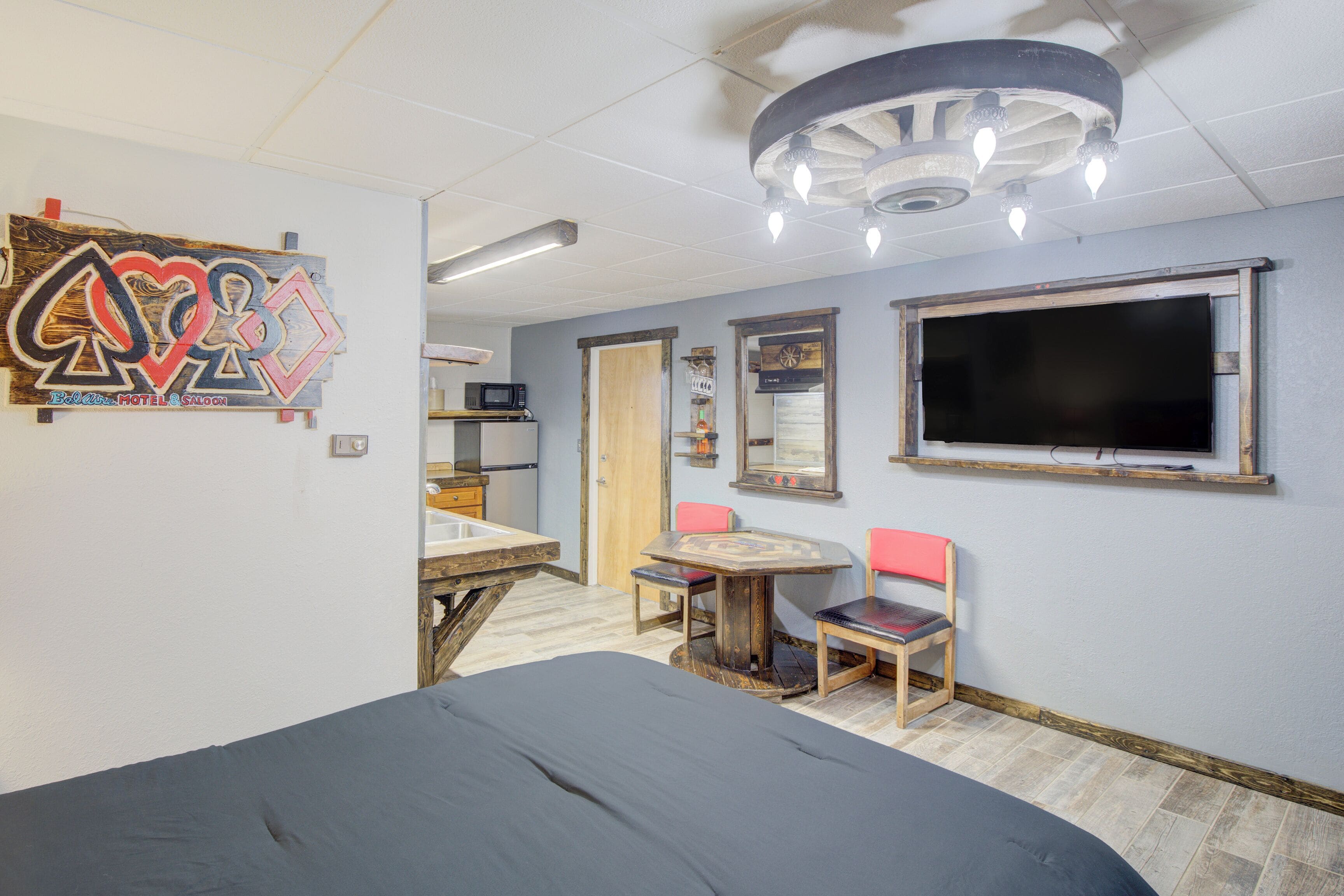 A room with a bed, a table with chairs, a TV, and a ceiling light fixture.