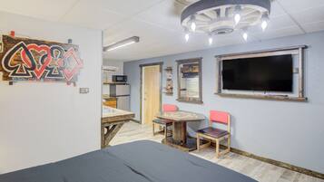 A room with a bed, a table with chairs, a TV, and a ceiling light fixture.