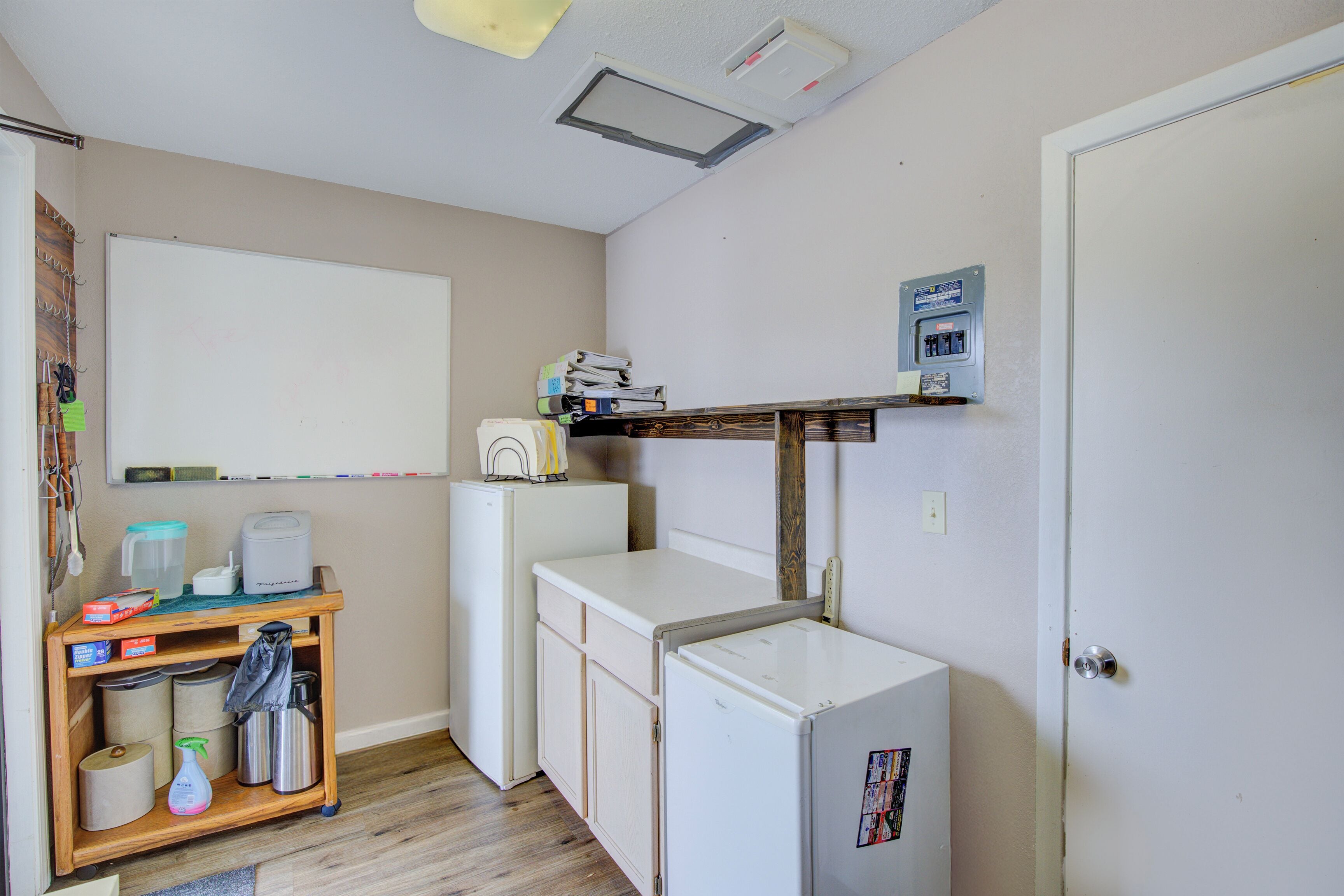 A compact kitchen with a white refrigerator, a small countertop, and a wooden shelf above the sink.