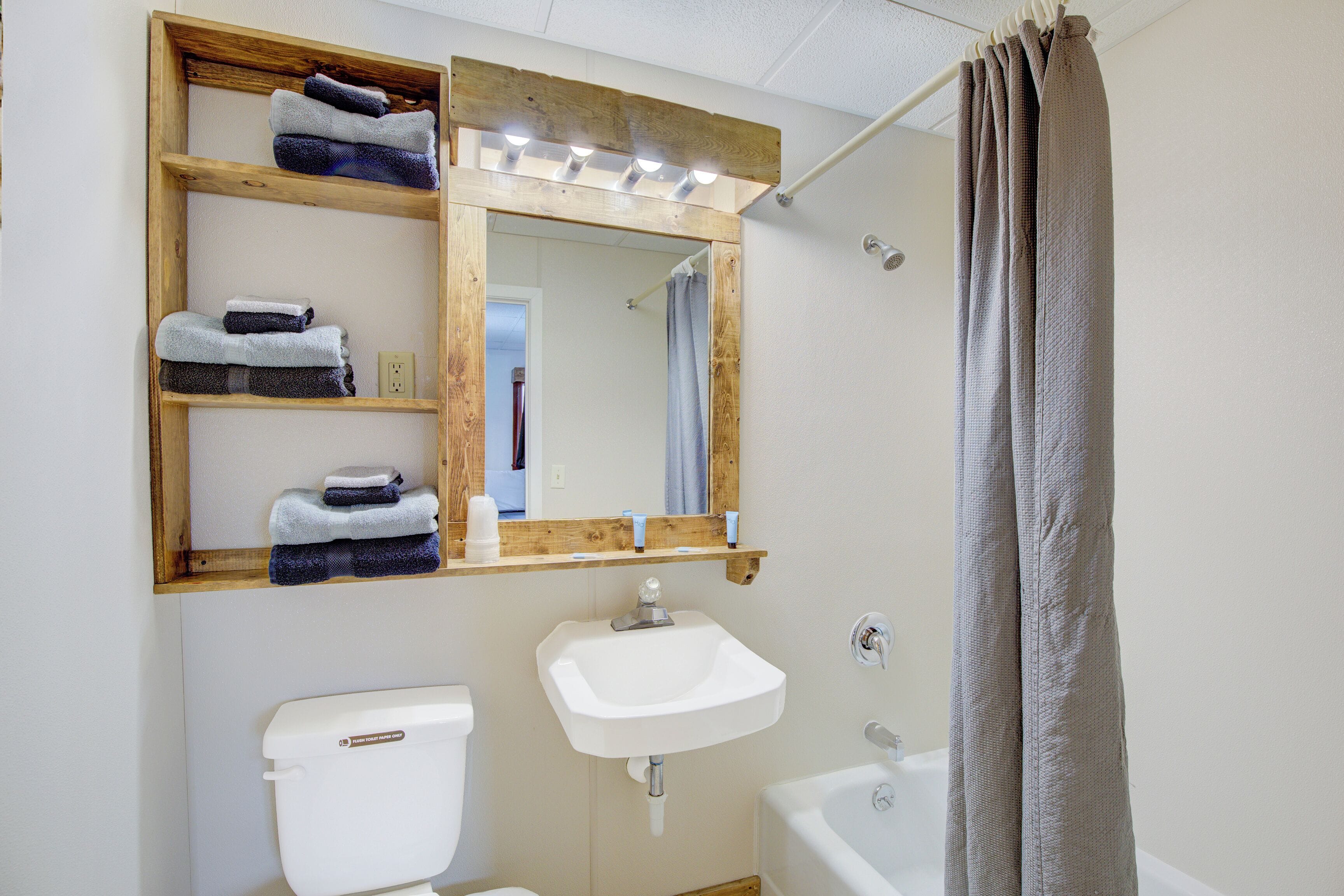 A bathroom with a wooden shelf holding towels, a sink, a toilet, and a bathtub.
