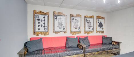 A room with a wooden bench with cushions, a red wall, and four framed playing cards on the wall.