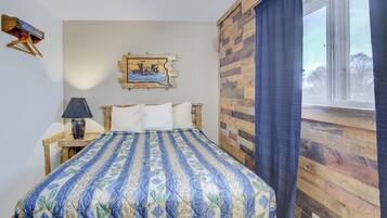 Quarto com cama, mesa de cabeceira, luminária, quadro na parede e janela com cortinas.