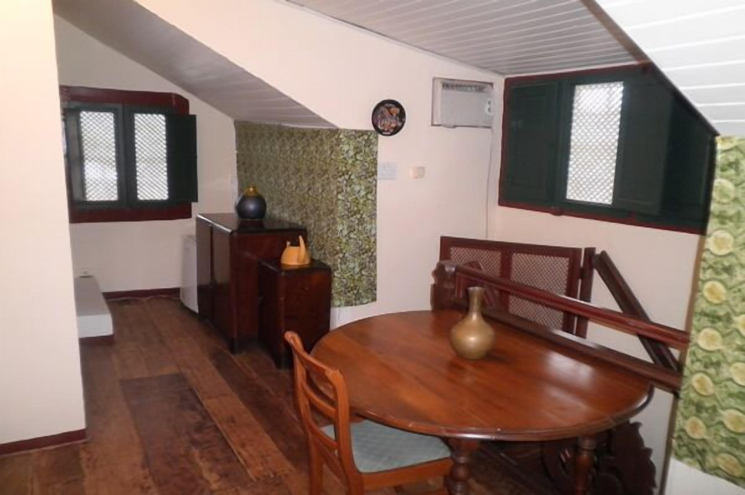 Un comedor con una mesa y sillas de madera, un florero y una ventana con contraventanas.