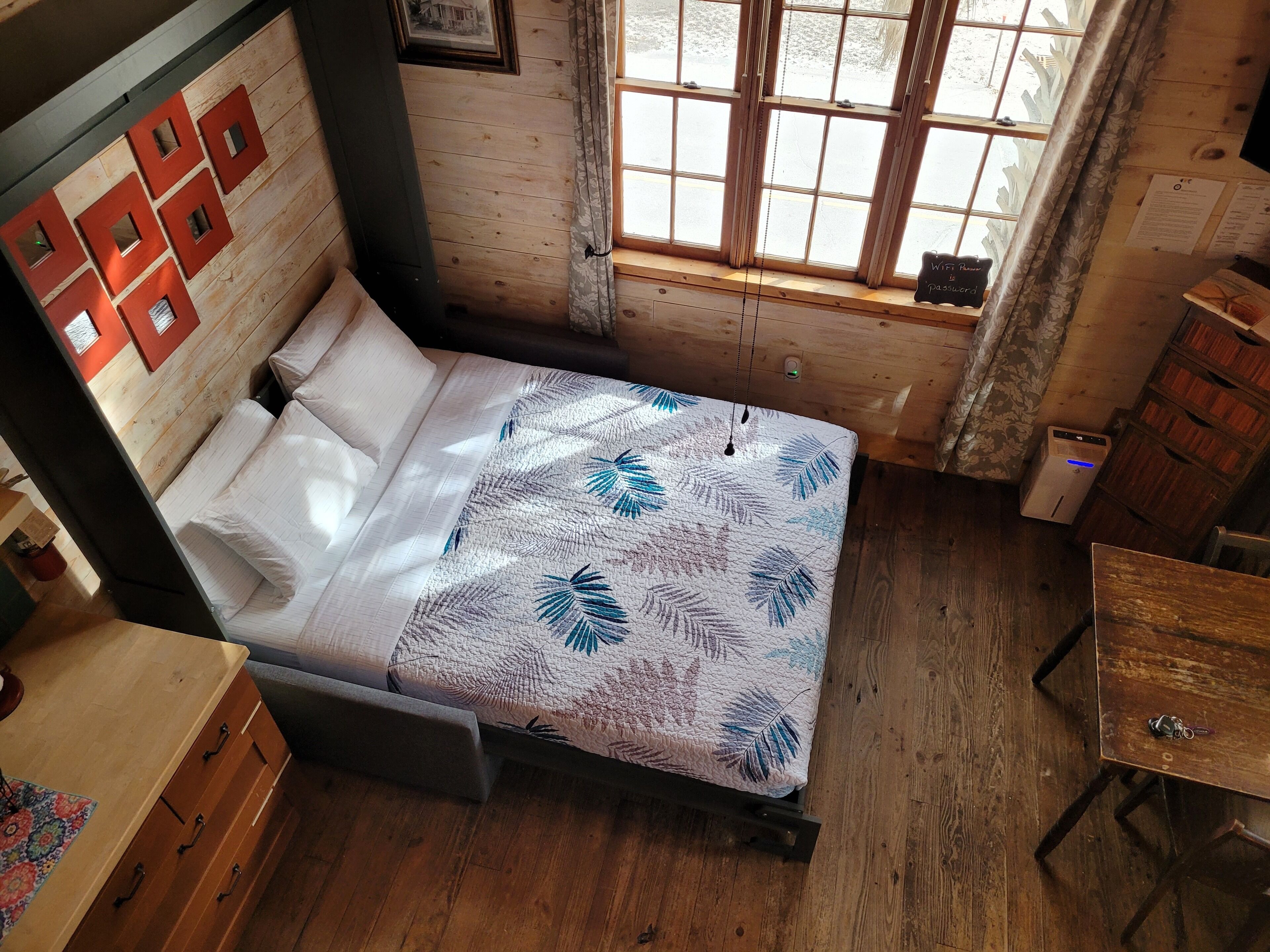 A wooden room with a bed, a desk, and a window.