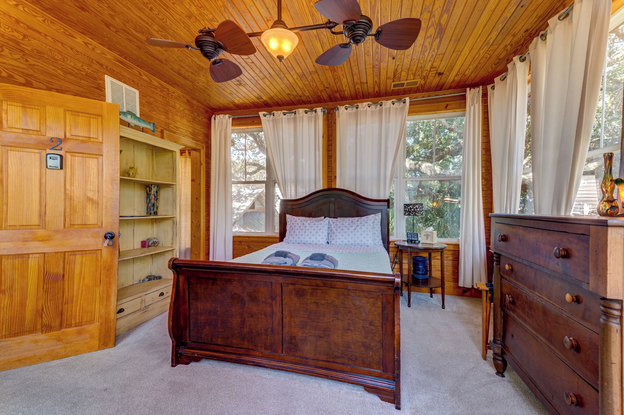 A wooden-paneled bedroom with a bed, a dresser, and a shelf unit.