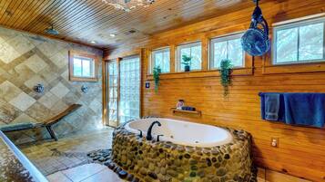 Un baño con bañera de piedra, paredes y techo de madera.