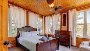 A wooden-paneled bedroom with a large bed, a dresser, and a nightstand. - Beachside Boutique Inn – Folly Beach Rooms & Private Cottages (Folly Beach)