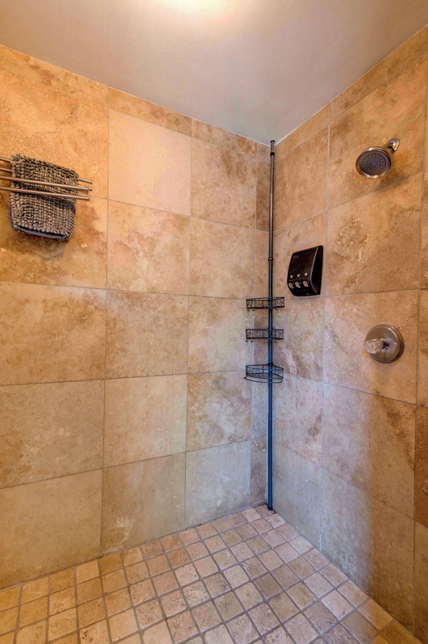 A corner shower with beige tiles, a metal showerhead, and a handheld shower attachment.