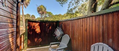 A wooden deck with two Adirondack chairs and a small table, surrounded by a wooden fence and trees.