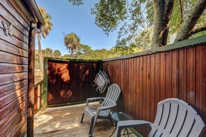 A wooden deck with two Adirondack chairs and a small table, surrounded by a wooden fence and trees.