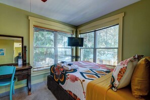 A bedroom with a bed, a desk, a chair, a television, and large windows. - Beachside Boutique Inn – Folly Beach Rooms & Private Cottages (Folly Beach)
