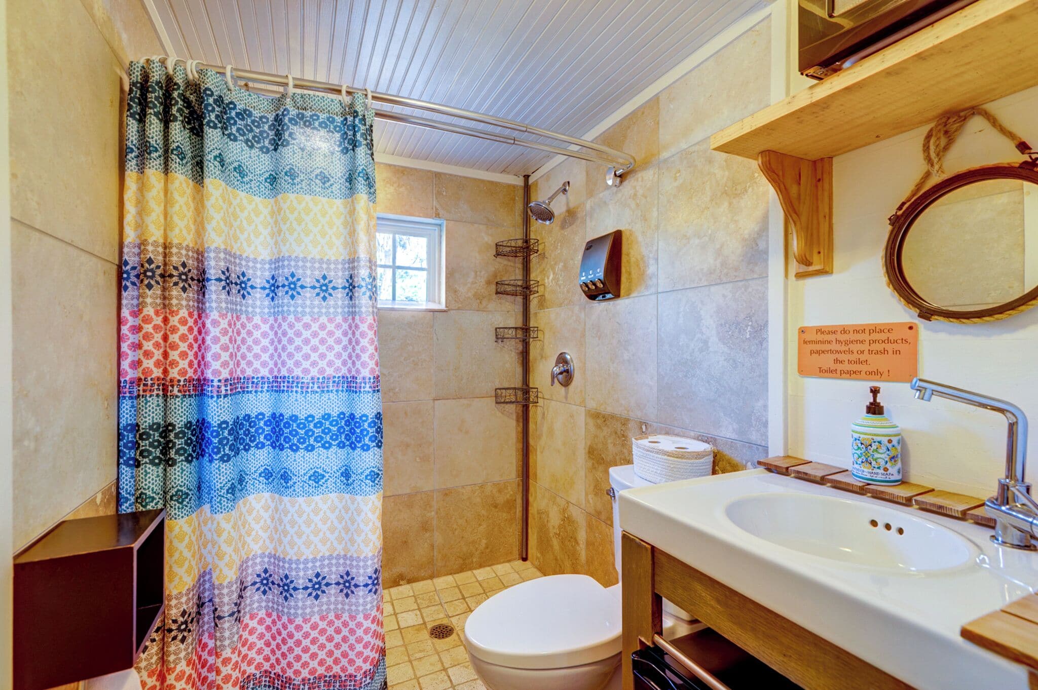 A bathroom with a shower, toilet, sink, and a sign instructing not to place feminine hygiene products in the toilet.