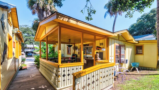A yellow building with a covered porch and a wooden deck. - Beachside Boutique Inn – Folly Beach Rooms & Private Cottages (Folly Beach)