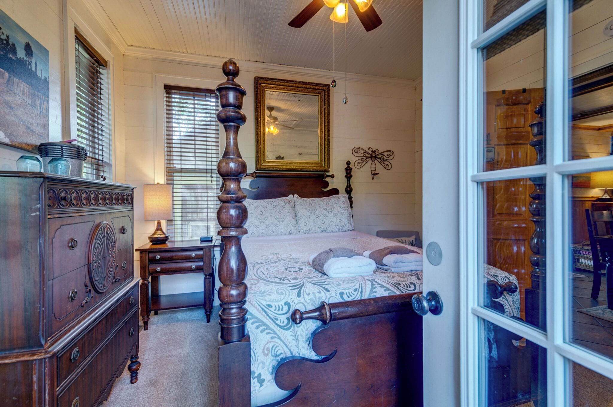 Une chambre à coucher avec un lit à baldaquin, une commode, une table de chevet et une fenêtre avec des stores.