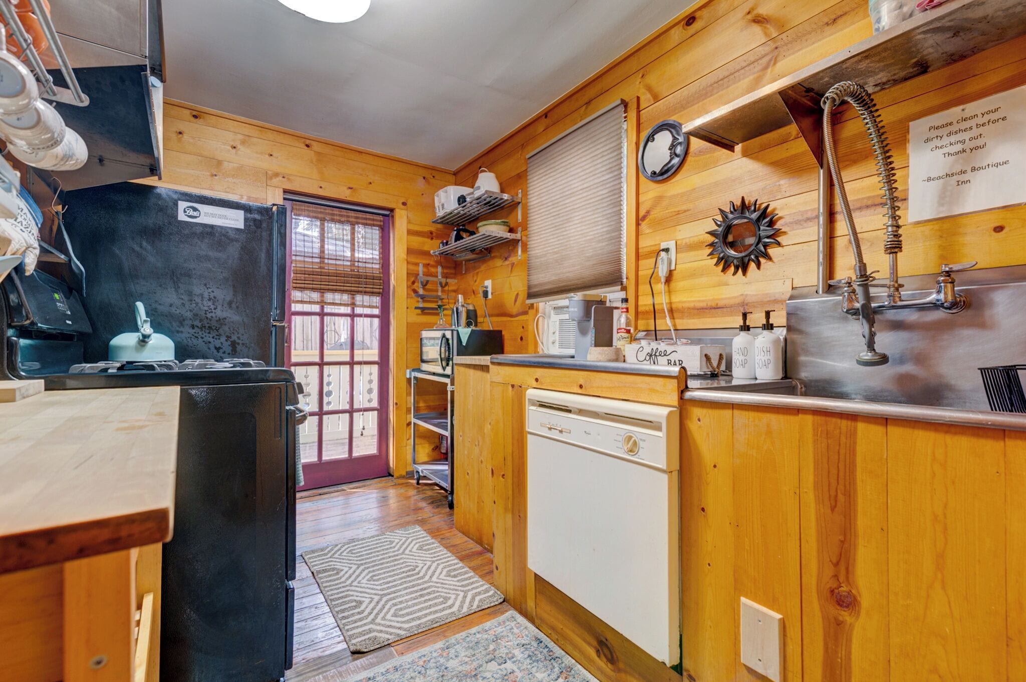 A compact kitchen with wooden walls, a refrigerator, a dishwasher, a sink, and a coffee station.