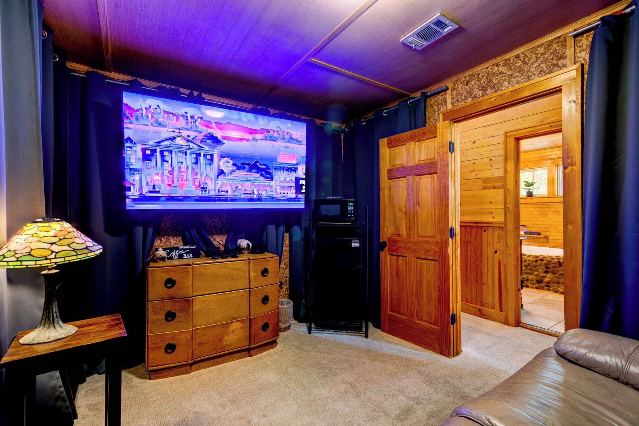 A cozy room with a large flat-screen TV, wooden furniture, and a stone wall.