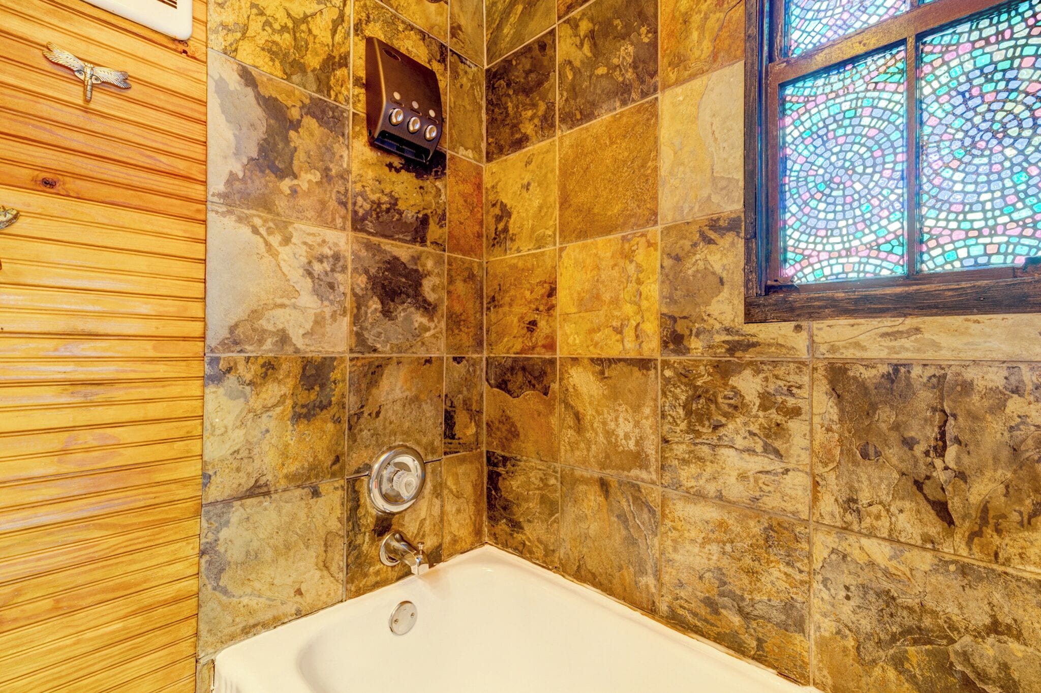 A bathroom with a bathtub, mosaic tiles, and a wooden panel wall.