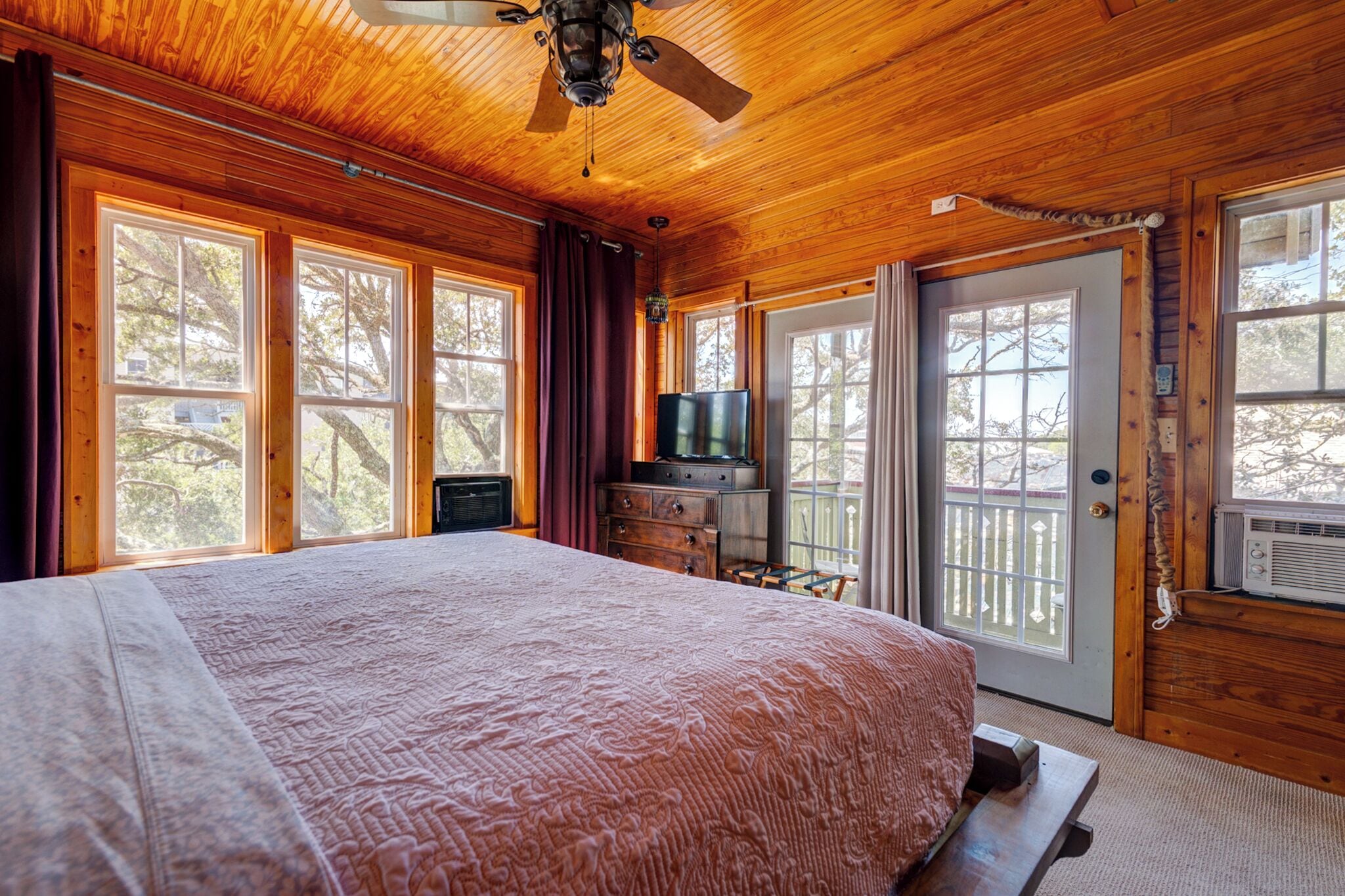 A wooden cabin bedroom with a large bed, a ceiling fan, and a television on a dresser.