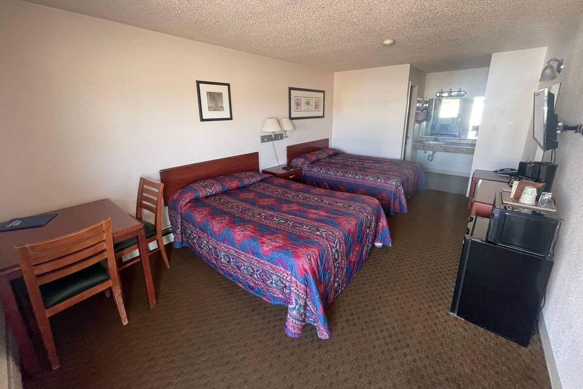 A hotel room with two beds, a desk, a chair, a small TV, and a bathroom visible through an open door.